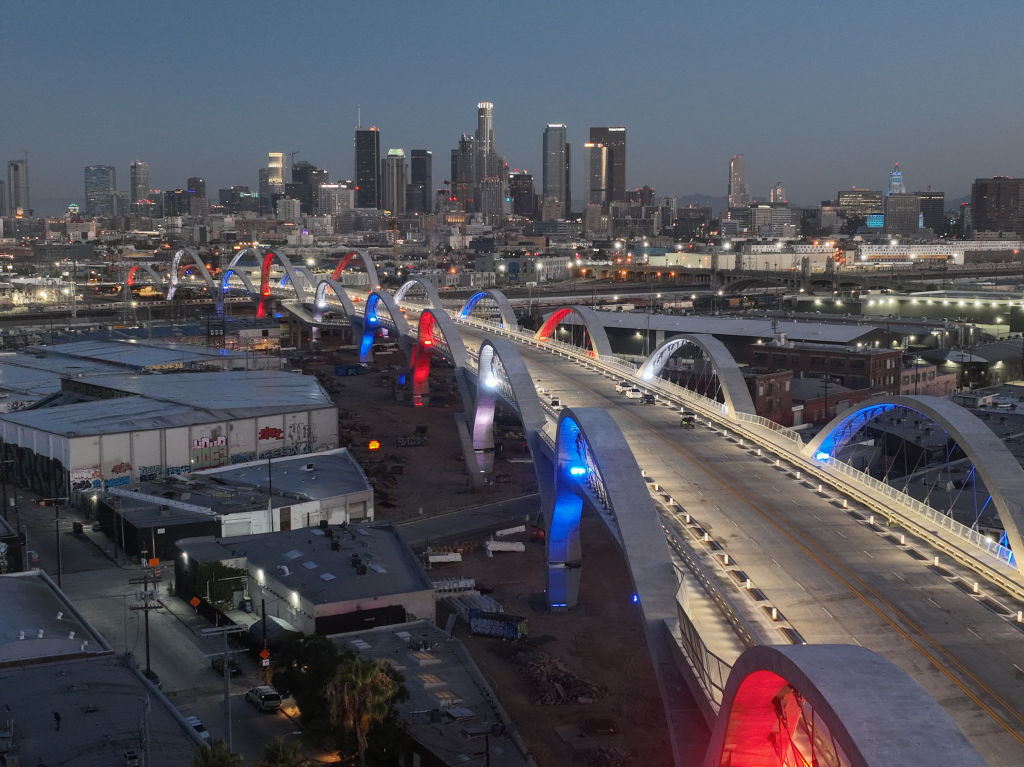A drone view at dawn of the downtown skyline and a side angle on the bridge arches majestically lit in red white and blue during the opening of the new 6th Street Bridge on July 10, 2022 in Los Angeles, California.  (Photo by Gary Leonard/Getty Images)